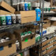 Storage shelf filled with spray paint cans and cardboard boxes in a workshop area.