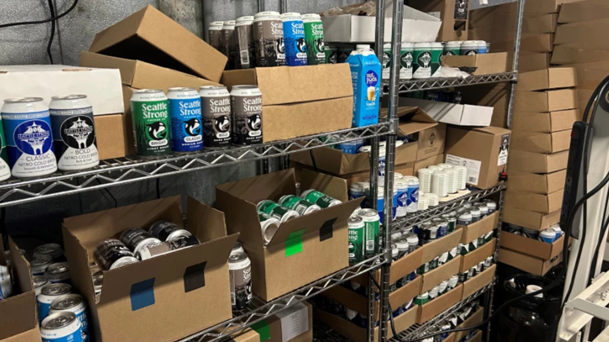 Storage shelf filled with spray paint cans and cardboard boxes in a workshop area.