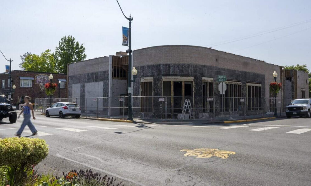 Street corner with a fenced storefront under renovation and ladders inside; pedestrians and parked cars nearby.