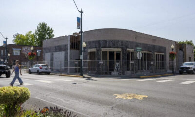 Street corner with a fenced storefront under renovation and ladders inside; pedestrians and parked cars nearby.