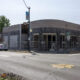 Street corner with a fenced storefront under renovation and ladders inside; pedestrians and parked cars nearby.