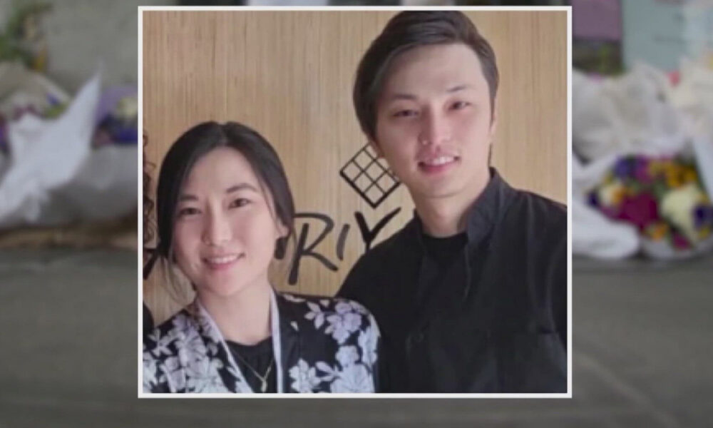 Two young adults, a woman and a man, smiling for a photo side by side indoors with a wooden backdrop behind them.
