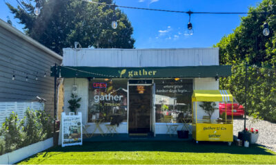 Small storefront with a green awning reading 'gather' and an Open sign; outdoor seating and a yellow 'gather & go' cart on the right, string lights above.