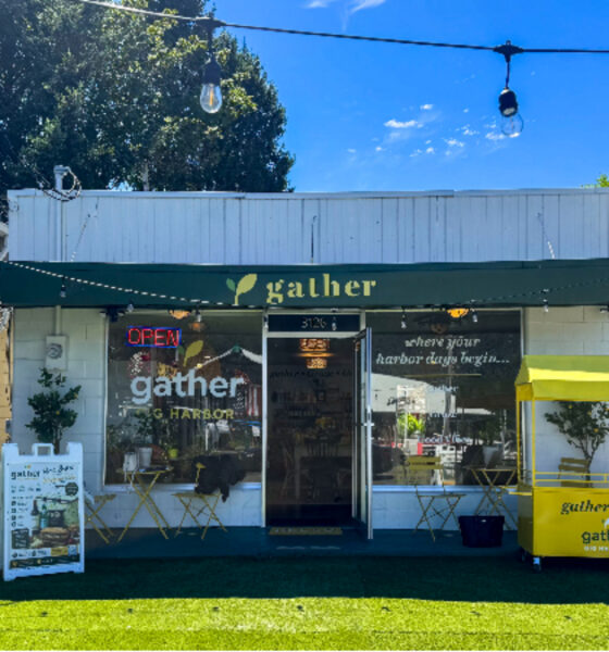 Small storefront with a green awning reading 'gather' and an Open sign; outdoor seating and a yellow 'gather & go' cart on the right, string lights above.