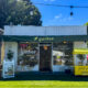 Small storefront with a green awning reading 'gather' and an Open sign; outdoor seating and a yellow 'gather & go' cart on the right, string lights above.