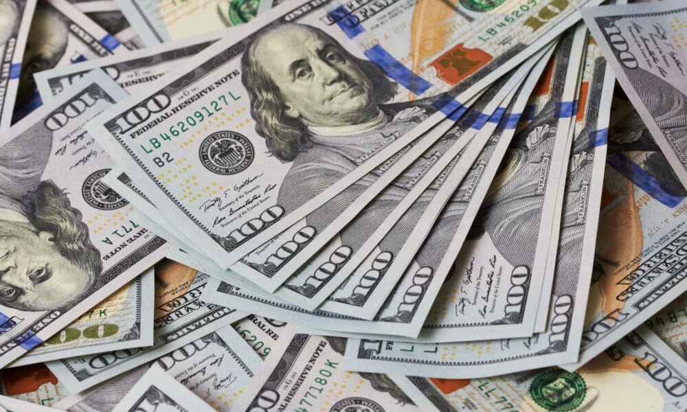 Pile of overlapping US $100 bills with Benjamin Franklin visible in the center.