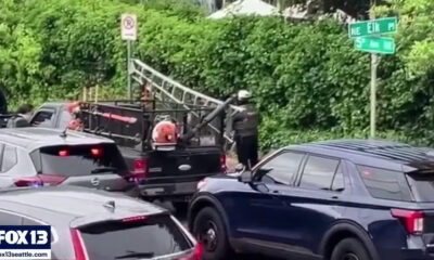 Emergency responders stand on the back of a black pickup with a long ladder extended, loading equipment on a crowded street; FOX13 logo in the lower-left corner.