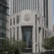 View of the King County Courthouse: a white stone building with a circular seal, flanked by tall glass skyscrapers, on a tree-lined street.