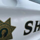 Side view of a white sheriff's cruiser with a large 'SHERIFF' decal and a gold star badge graphic.