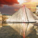Glass pyramid lit at dusk in the Louvre Courtyard, with the historic building and reflecting pool nearby.