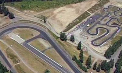 Aerial view of a go-kart track with winding black asphalt curves and surrounding trees.