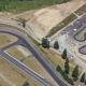 Aerial view of a go-kart track with winding black asphalt curves and surrounding trees.