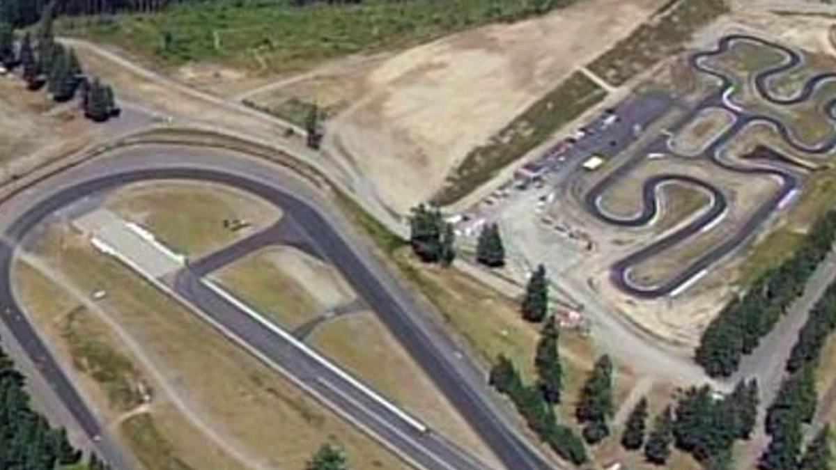 Aerial view of a go-kart track with winding black asphalt curves and surrounding trees.