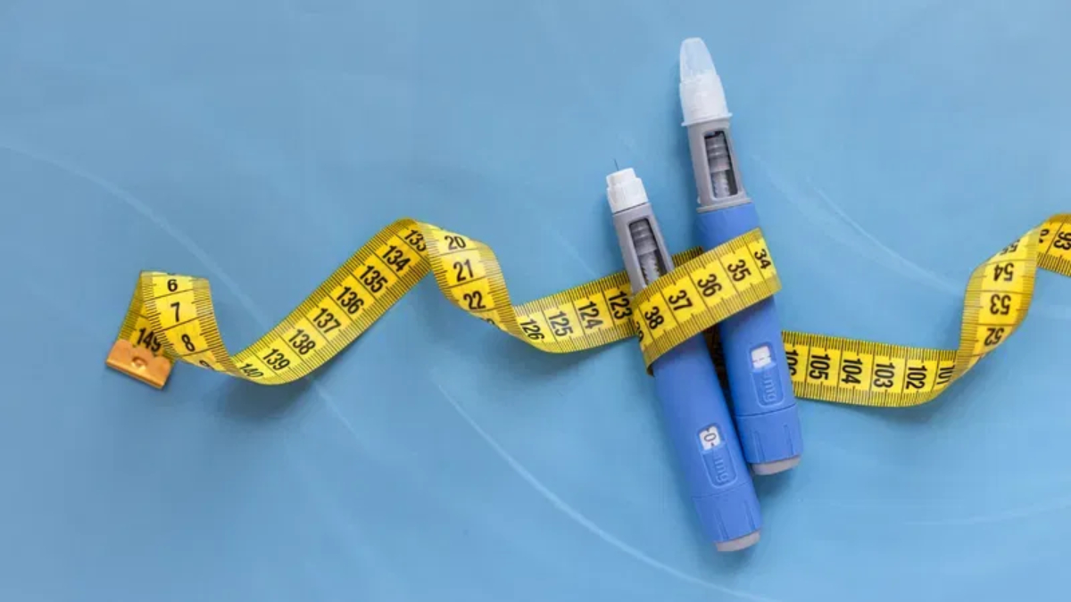 Two blue insulin pens with a yellow measuring tape draped around them on a blue background, symbolizing diabetes management.