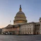 Wide-angle view of the U.S. Capitol in Washington, D.C. with its dome lit at sunset and grand neoclassical wings on either side, plus steps in the foreground.