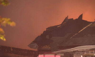 Charred roof of a building with flames glowing in the background.