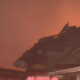 Charred roof of a building with flames glowing in the background.