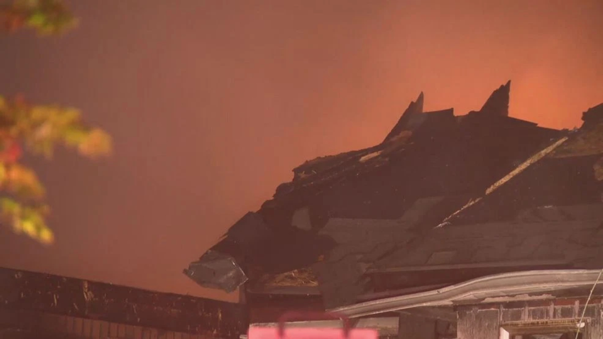 Charred roof of a building with flames glowing in the background.