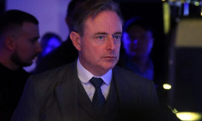 Middle-aged man in a gray suit and polka-dot tie at a dim, blue-lit event, looking to the right.
