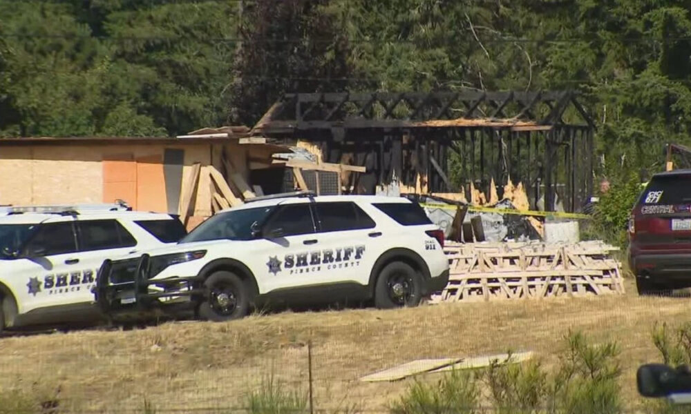 Two sheriff patrol vehicles parked outside a partially burned building under construction with plywood debris and caution tape in view.