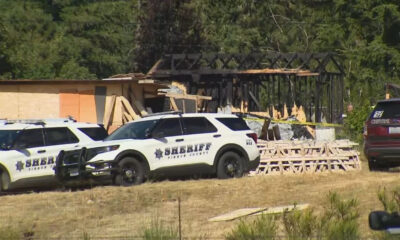 Two sheriff patrol vehicles parked outside a partially burned building under construction with plywood debris and caution tape in view.
