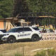 Two sheriff patrol vehicles parked outside a partially burned building under construction with plywood debris and caution tape in view.