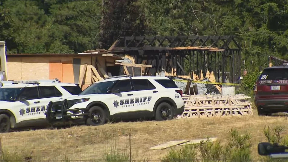 Two sheriff patrol vehicles parked outside a partially burned building under construction with plywood debris and caution tape in view.