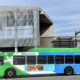 Public transit bus (Pierce Transit) green and blue, driving past a modern, mesh-covered building on a city street.