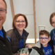 A family of four posing for a selfie in an airport terminal before their flight, smiling at the camera.