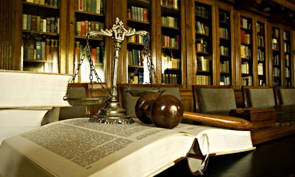 Open law book with a gavel and scales of justice on a dark table in a law library setting