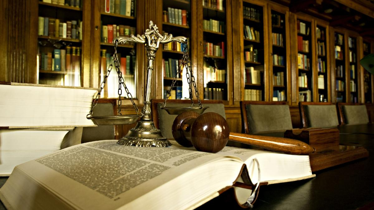 Open law book with a gavel and scales of justice on a dark table in a law library setting