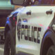 Police SUV with POLICE lettering and shield logo at a crime scene, yellow caution tape in the background.