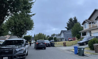 Residential street blocked off with yellow police tape; police vehicles and a few officers present in front of houses.
