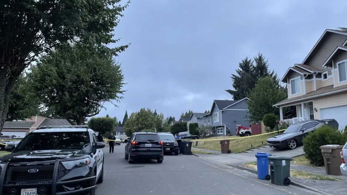 Residential street blocked off with yellow police tape; police vehicles and a few officers present in front of houses.