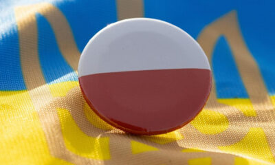 Round pin badge showing the Polish flag (white over red) on a blue and yellow fabric background.