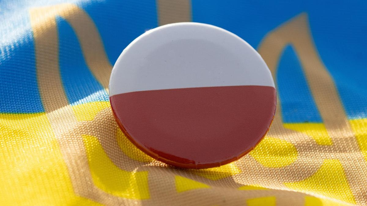 Round pin badge showing the Polish flag (white over red) on a blue and yellow fabric background.
