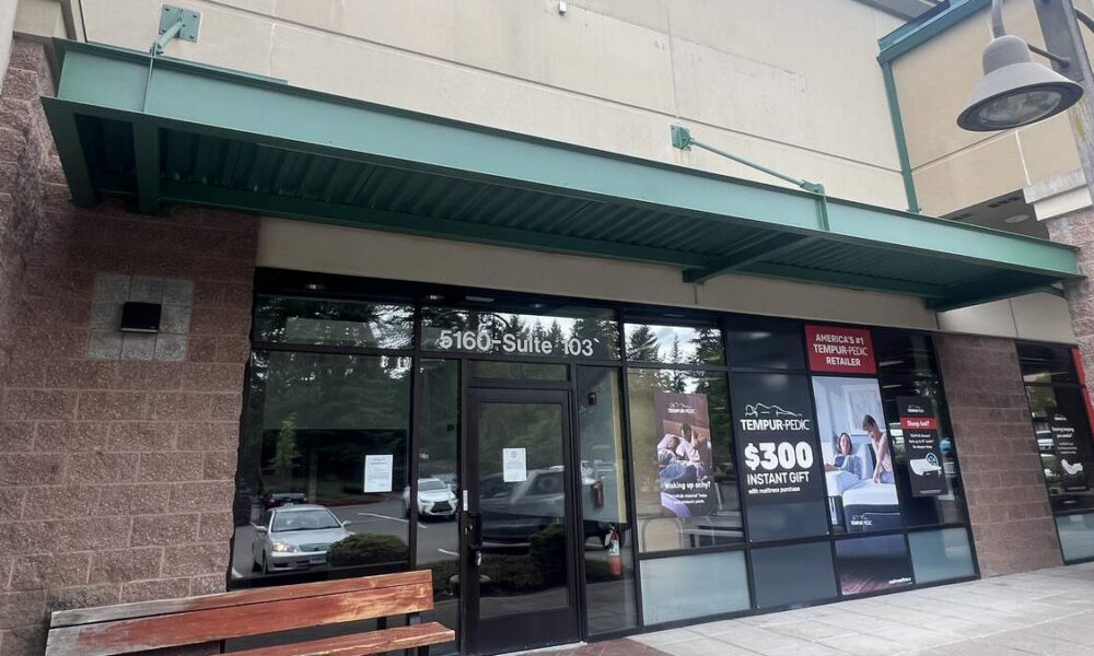 Storefront with glass entrance under a green awning; sidewalk bench on the left and promotional posters in the windows.