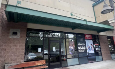 Storefront with glass entrance under a green awning; sidewalk bench on the left and promotional posters in the windows.