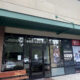 Storefront with glass entrance under a green awning; sidewalk bench on the left and promotional posters in the windows.