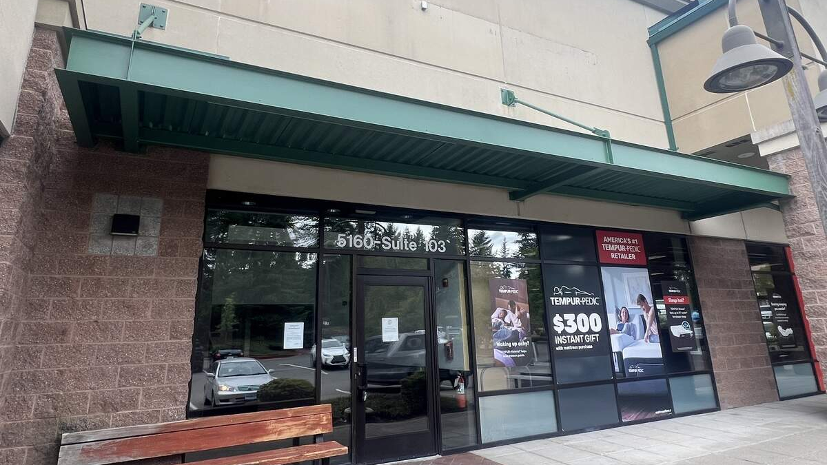 Storefront with glass entrance under a green awning; sidewalk bench on the left and promotional posters in the windows.