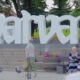 Large white Dubai sign sculpture in a park with steps, greenery, and people sitting on benches nearby.