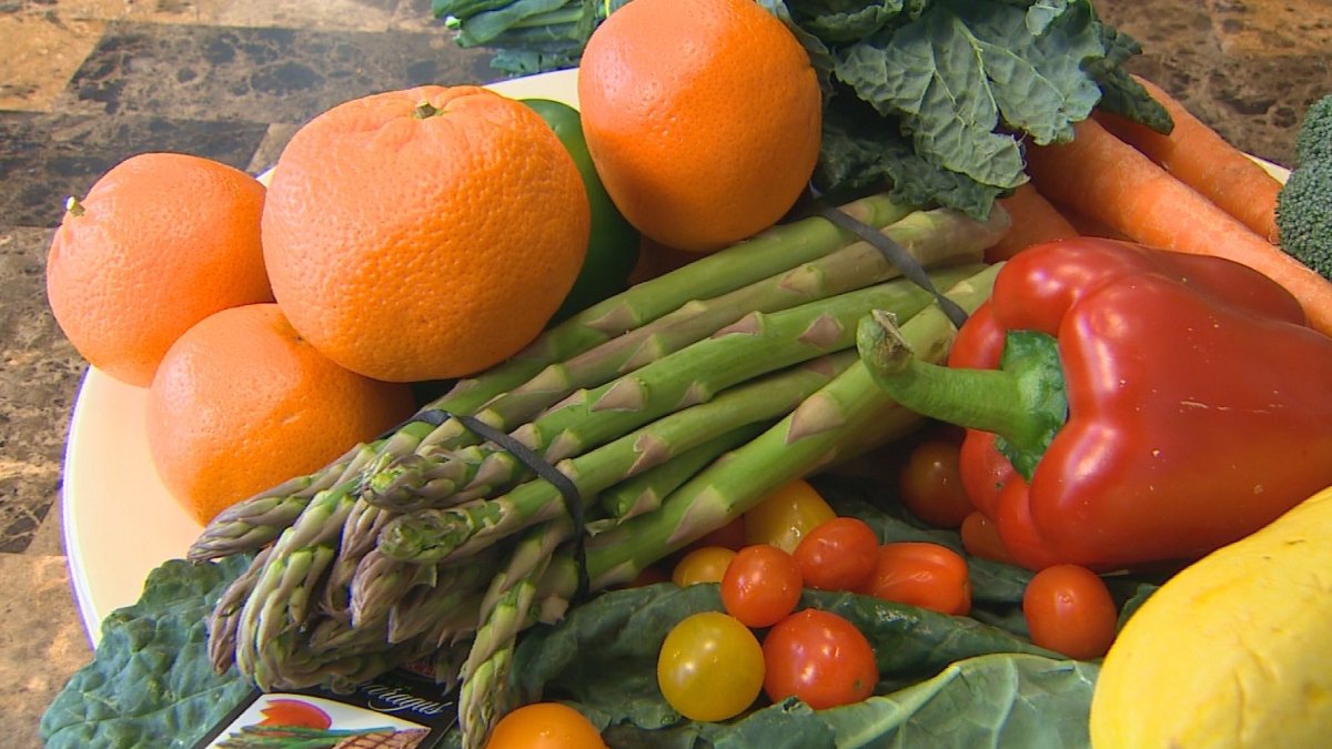 Assorted fresh vegetables and fruits: oranges, asparagus, a red bell pepper, cherry tomatoes, leafy greens, carrots, and broccoli on a plate.