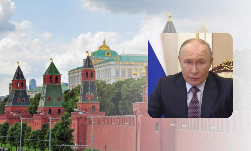 View of the Kremlin towers and red brick wall against a blue sky, with a rounded inset showing a man in a suit speaking in a formal setting.
