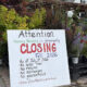 Sign at a plant nursery announcing permanent closing in Fall 2026, with bullet points about sales, returns, exchanges, and guarantees, surrounded by potted plants and flowers.