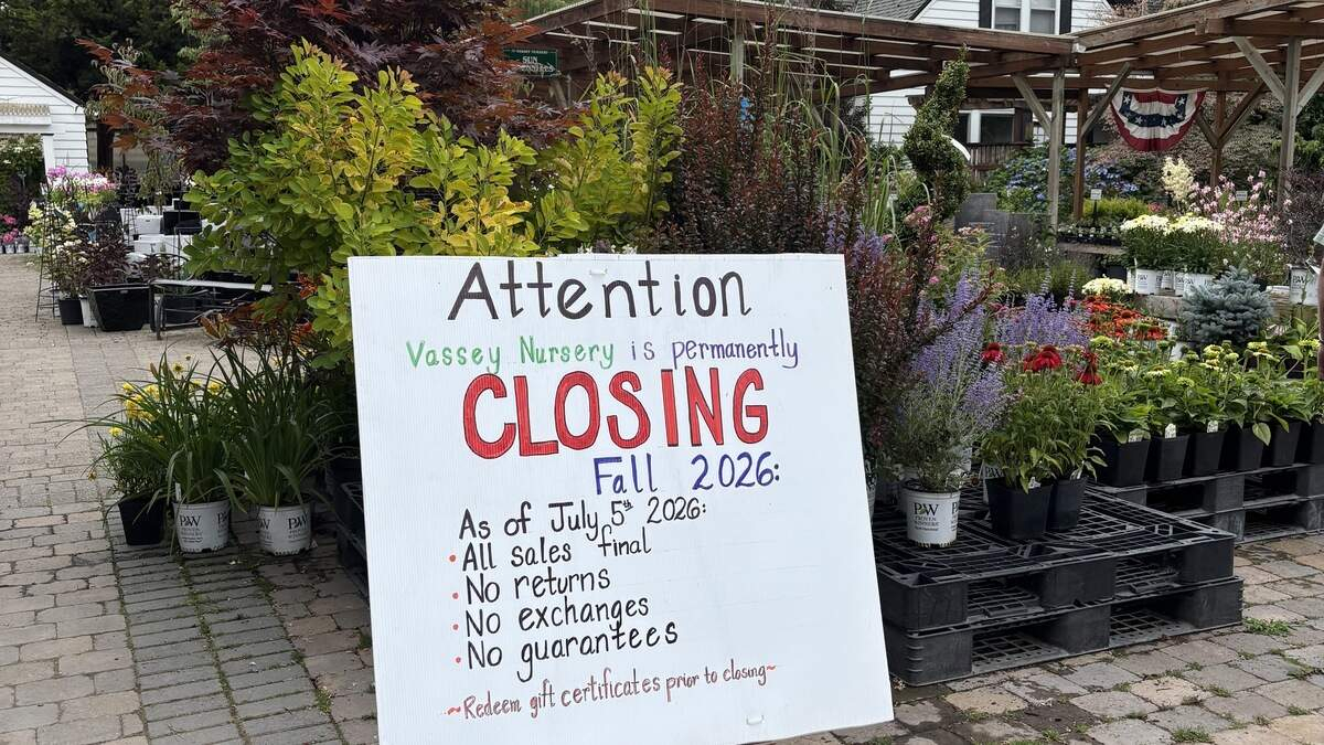 Sign at a plant nursery announcing permanent closing in Fall 2026, with bullet points about sales, returns, exchanges, and guarantees, surrounded by potted plants and flowers.