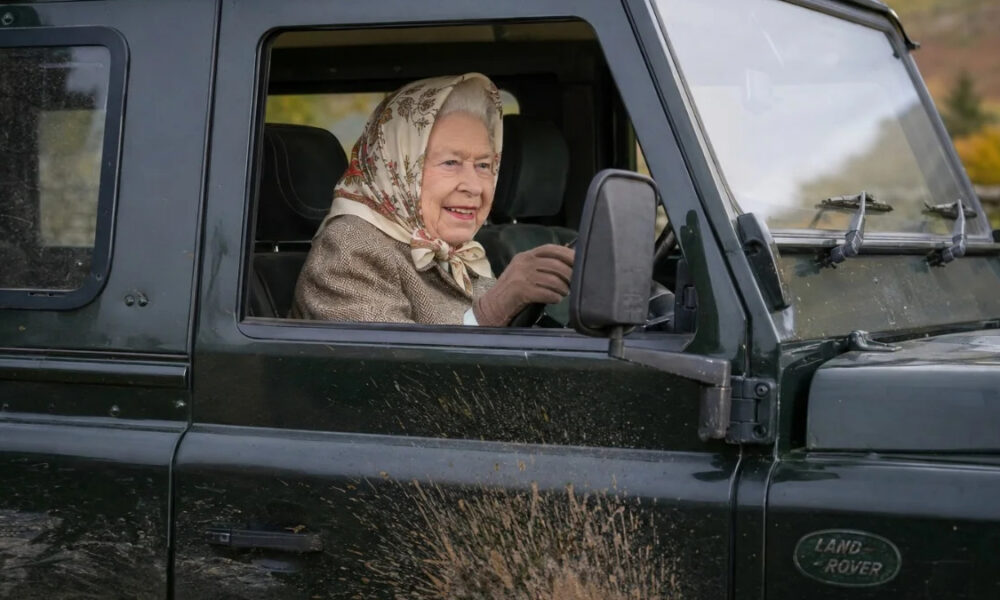 Older woman wearing a patterned headscarf driving a black Land Rover, mud splattered on the door.