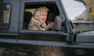 Older woman wearing a patterned headscarf driving a black Land Rover, mud splattered on the door.