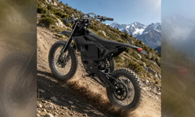 Black electric dirt bike on a rocky mountain trail with snow-capped peaks in the distance.