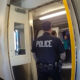 Two police officers stand at an open subway car door; one facing away with 'POLICE' on his back and another officer on the left.