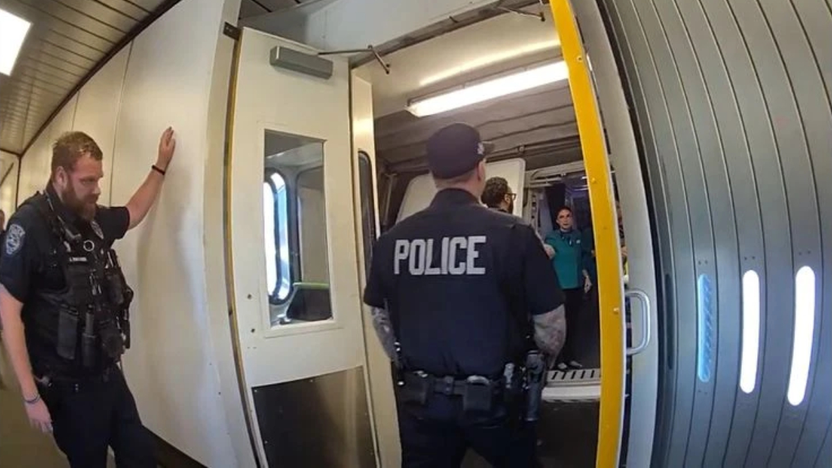 Two police officers stand at an open subway car door; one facing away with 'POLICE' on his back and another officer on the left.
